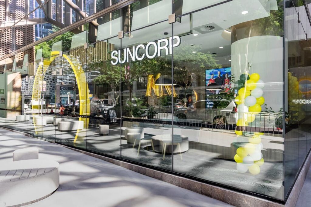 Glass-fronted Suncorp branch with modern interior, yellow and white balloons, and seating. City street reflection visible in the glass.